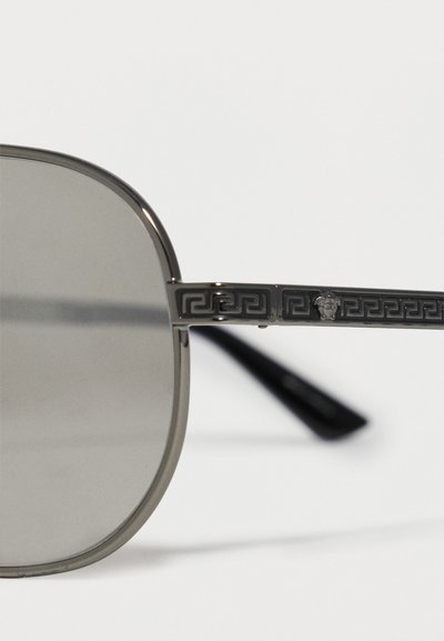 Σκελετός γυαλιών ηλίου με σκούρους αποχρωματισμένους στρογγυλούς φακούς και ανάγλυφο μοτίβο ελληνικού κλειδιού στα μεταλλικά βραχίονες, με ένα μικρό έμβλημα κεφαλής Μέδουσας.