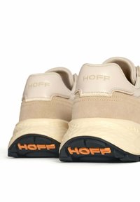 Zapatillas beige con un upper texturizado y acentos de ante, una suela media gruesa en color crema y una suela exterior negra con el logo naranja "HOFF".