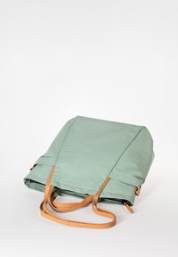 Groene waterdichte rugzak met tan leren banden, een omvouwbare flap en een reliëflogo aan de voorkant. Vlakke en rechthoekige vorm.