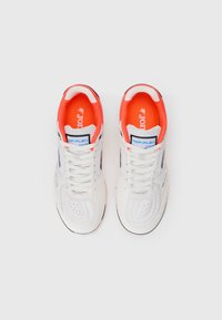 Białe sneakersy z pomarańczowymi akcentami, cholewka wykonana z tkaniny i syntetyku, perforowany nos, sznurowadła i wyściółka z amortyzacją. Posiadają oznaczenie "TOP-FLEX".