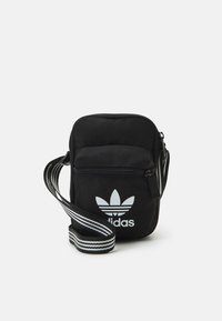 Borsa a tracolla nera in tessuto con chiusura a zip, caratterizzata da un logo adidas bianco e una tracolla regolabile a righe. Forma rettangolare compatta.