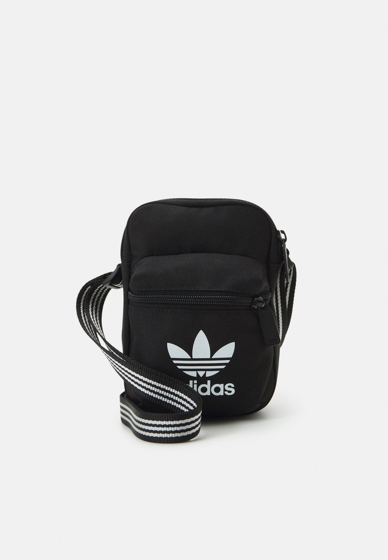 Borsa a tracolla nera in tessuto con chiusura a zip, caratterizzata da un logo adidas bianco e una tracolla regolabile a righe. Forma rettangolare compatta.