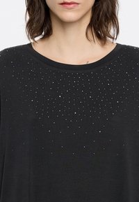 Zwart T-shirt met korte mouwen en een ronde halslijn, versierd met verspreide zilveren kralen op de bovenste helft. Soepele stofstructuur.