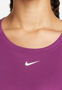 Lila sporttop med rund halsringning. Har en vit Nike-logotyp på vänster bröst. Slät textur och figurnära design.