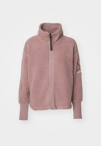 Chaqueta de forro polar en rosa suave, con un cuello alto, cierre de media cremallera en la parte delantera y puños acanalados. Detalle de parche cuadrado en el brazo izquierdo. Textura suave.