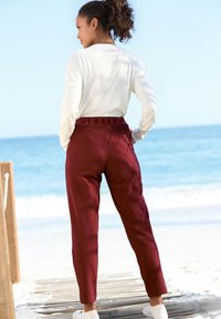 Bordeauxfarbene, schmal zulaufende Hosen mit einem elastischen Bund und Logodetail, kombiniert mit einem weißen Langarmshirt. Glatte Stoffstruktur.