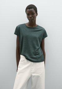 Donkergroene katoenen t-shirt met ronde hals en korte mouwen, gecombineerd met witte broeken. Gladde textuur, casual pasvorm, minimalistisch ontwerp zonder patronen.