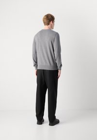Herren Grauer Strickpullover mit Rundhalsausschnitt, gerippten Bündchen und Saum. Kombiniert mit schwarzen, locker sitzenden Hosen und schwarzen Schuhen.