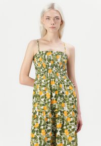 Robe florale verte avec un bodice smocké, présentant des motifs d'oranges et de citrons et des fines bretelles. La jupe a un design en niveaux.