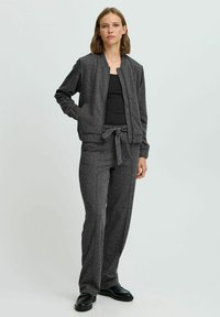 Veste bomber grise avec fermeture éclair à l'avant et poches latérales, associée à un pantalon large assorti avec une taille à nouer. Texture lisse.