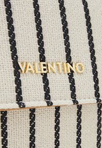 Canvas handbag with black stripes on a cream background. Features a gold "Valentino" logo. Textured fabric with stitched detailing.