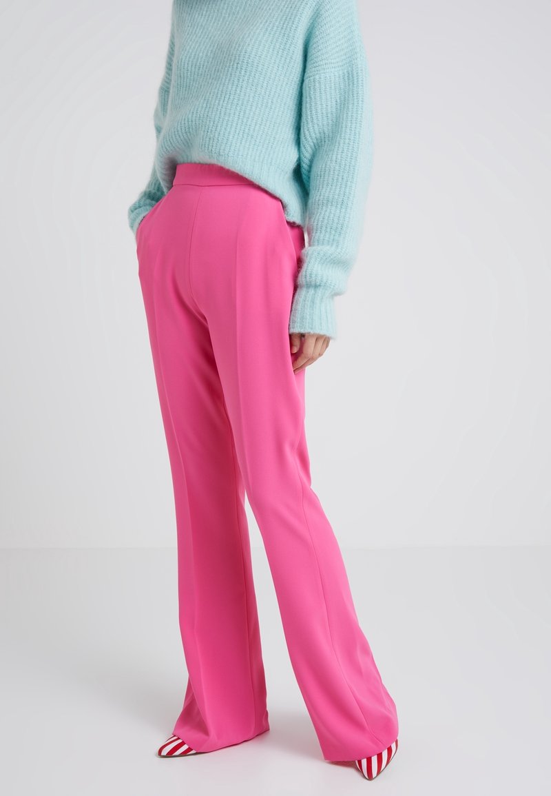 Personne portant un pantalon droit rose vif, un pull bleu clair duveteux et des chaussures pointues à rayures rouges et blanches sur un fond uni.