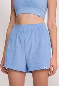 Ljust blå frottéshorts med elastisk midja, med en liten märkesetikett. Tygmaterialet verkar mjukt med en slät struktur.
