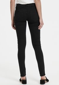 Černé úzké džíny s vysokým pasem, které mají dvě zadní kapsy, štíhlý střih a hladký povrch, doplněné černými vysokými podpatky.