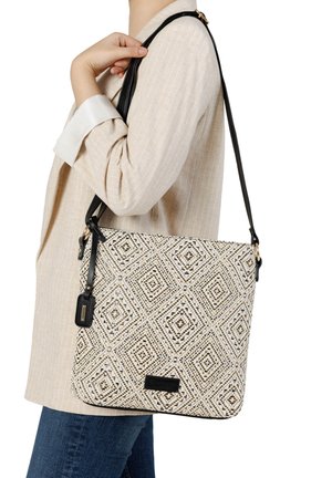 Personne portant un blazer beige et un jean, portant un grand sac à bandoulière tissé avec un motif noir et blanc et une sangle noire.