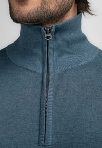 Aangesloten trui met een hoge kraag van zacht blauwe stof, met een rits in het midden en geribbelde textuur langs de nek en manchetten.