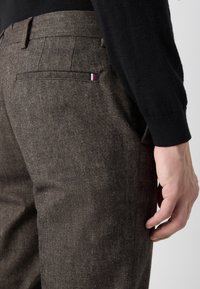 Pantaloni in tweed marrone con una finitura testurizzata, dotati di tasca posteriore e piccole strisce tricolori come accento. Vestibilità sartoriale con gamba affusolata.