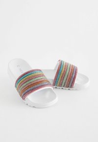Fehér talpú, csúsztatós szandál, multiszínű, csíkos textil felsőrésszel. A pánt sima tapintású, változó szélességű csíkokkal rendelkezik.