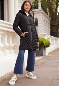Chaqueta acolchada negra con capucha, cierre de cremallera y bolsillos laterales. Combinada con unos vaqueros de campana cortos y zapatillas blancas con estampado de leopardo.
