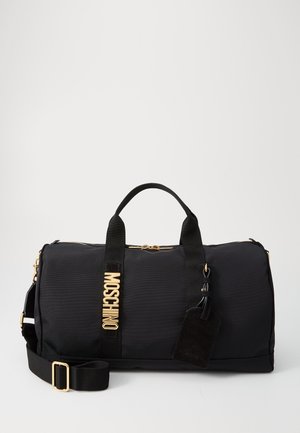 Black nylon duffel bag with gold hardware, featuring dual top handles, adjustable shoulder strap, and stitched logo patch. Textured surface.