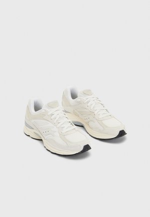 Weiße Sportschuhe mit Obermaterial aus Mesh, verstärkter Zehenkappe, gepolsterter Sohle und dezenten grauen Akzenten an den Seiten und der Ferse. Schnürdesign.