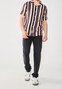 Korte mouwen shirt met verticale strepen in crème, marineblauw en bordeauxrood. Zwarte jeans en witte sneakers met grijze accenten maken de outfit compleet.