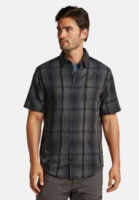 Chemise à manches courtes à carreaux en gris foncé et noir, avec un col boutonné, une poche à rabat et un tissu structuré avec des motifs de grilles variés.