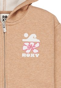 Sudadera con cremallera color beige con un gráfico de ola blanca y flor rosa. Textura de tela suave con capucha de doble capa y cremallera frontal.