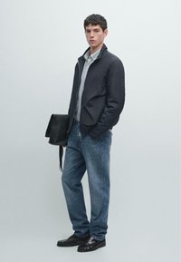 Czarna nylonowa kurtka bomberka, koszulka w paski, niebieskie dżinsy, czarne skórzane buty oraz czarna torba na ramię. Gładkie tekstury i swobodny krój.