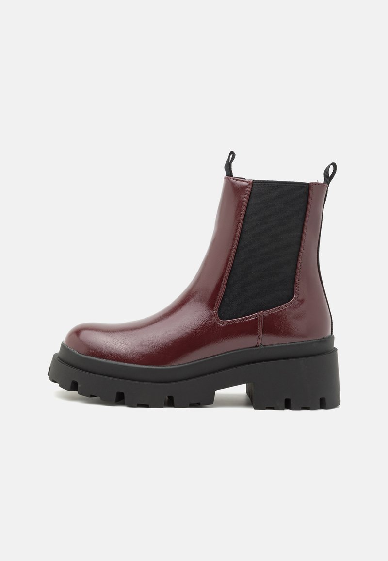 Bottines en cuir verni bourgogne avec une semelle noire épaisse, des panneaux latéraux en élasthanne et des languettes de tirage, présentant un design imposant et robuste.