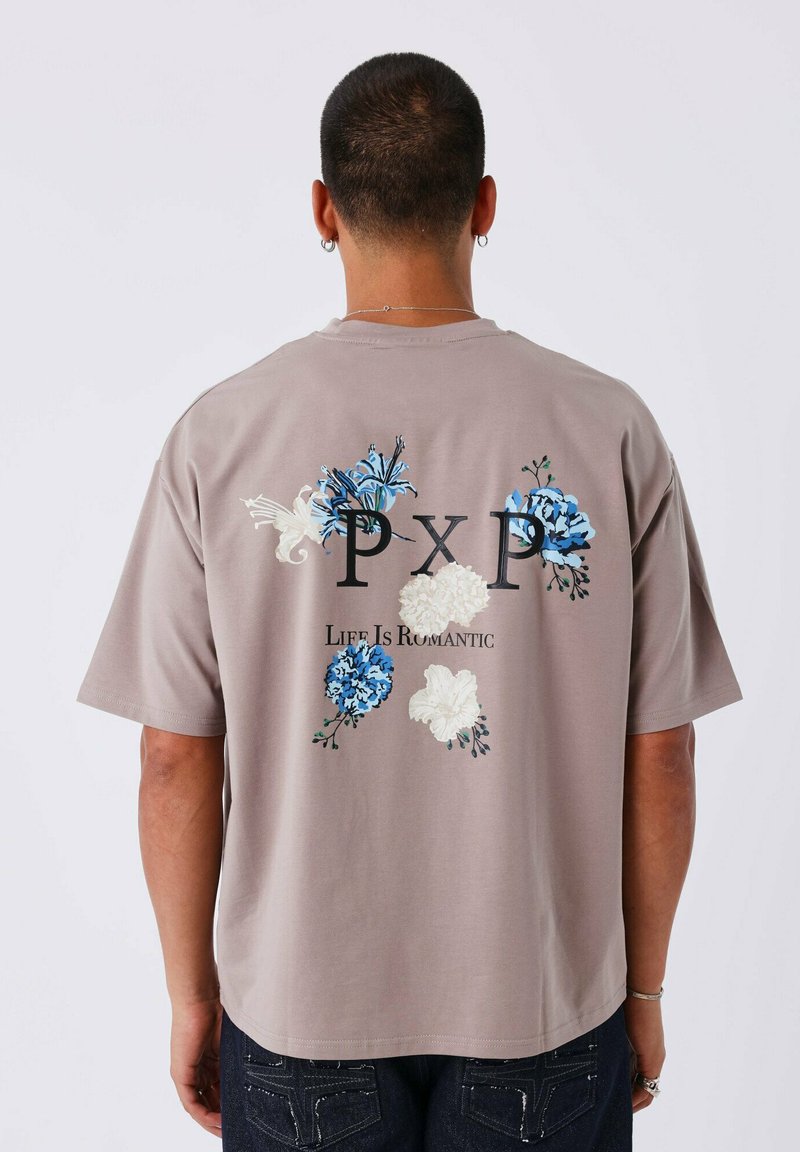 Camiseta gris de manga corta con embellishments florales en azul y blanco, con el texto "PXP La Vida Es Romántica" en negro.