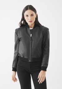 Černá kožená bomber bunda s ribovanými manžetami a lemem, se zapínáním na přední zip a hladkou texturou. Nosená přes bílý top.