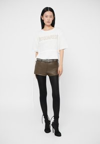 Witte korte mouw t-shirt met "DSQUARED2" bedrukt in beige, gecombineerd met olijfgroene leren shorts, zwarte legging en zwarte sandalen met bandjes.
