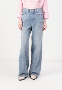 Light blue denim jeans with heart patterns. Features a high waist, wide-leg cut, and slight distressing, paired with a pink button-up shirt.
