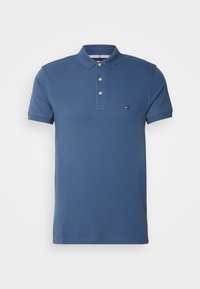 Polo bleu à manches courtes avec trois boutons et petit logo rouge, blanc et bleu sur la poitrine gauche.