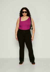 Prilagojen vijoličen top z enim ramenom v kombinaciji s črnimi hlačami z visokim pasom. Manekenka nosi črne sončna očala in nosi majhno črno torbico.