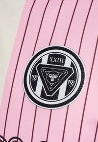 Rosa og cremefarvet stribet stof med en cirkulær sort-hvid logo med et trekantet design, "XXIII" og forskellige former.