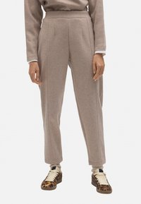 Pantalones de mezcla de lana beige con una cintura alta, que cuentan con costuras verticales y pierna ajustada. Combinados con zapatillas de deporte con estampado.