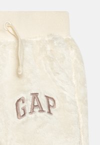 Kremskrāsas vilnas joggeri ar ribotu jostasvietu un izsistu "GAP" logo gaiši brūnā krāsā. Aprīkoti ar auklu jostasvietā.