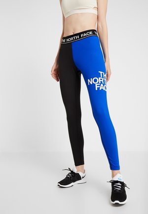 Collants avec un design en blocs de couleurs, noir à gauche et bleu à droite, avec un logo blanc "The North Face" sur le côté bleu.