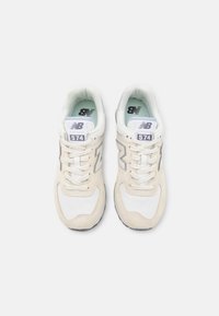 Paire de baskets New Balance 574 beige et blanches avec des lacets blancs vues de dessus sur fond blanc.