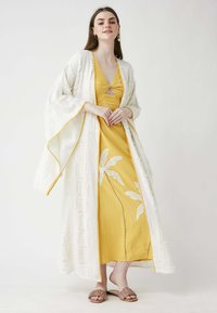 White embroidered kimono over a yellow dress with leaf patterns, featuring a V-neck and split hem, paired with tan flat sandals.