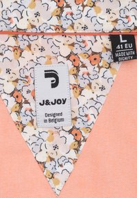 Stoflabel met bloemenpatroon in tinten van crème, oranje en bruin, met een driehoekig ontwerp. Inclusief product- en merklabels.