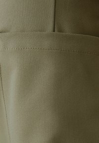 Khaki látka s hladkou strukturou, se viditelným švem a plochým designem kapsy. Barva je tlumená olivově zelená.