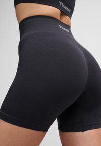 Hoch taillierte schwarze Sportshorts aus elastischem Stoff, mit gerippter Textur und dezentem Logo-Detail am Bund.