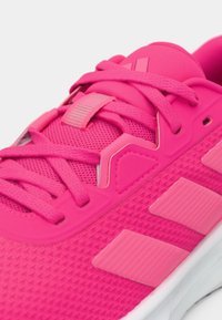 Chaussure de sport rose vif avec dessus texturé, lacets assortis et accents de design angulaires. Dispose d'une semelle blanche et de détails réfléchissants.