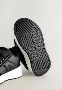 Baskets noires avec une semelle en caoutchouc texturé présentant un motif en zigzag et des grips circulaires, une semelle intermédiaire blanche et un dessus en synthétique lisse.