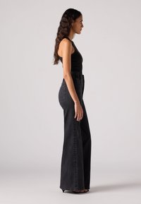 Zwarte tanktop gecombineerd met hoge taille, wijde zwarte jeans, met een gladde textuur en een strakke silhoeet.