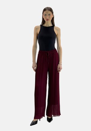 Zwarte mouwloze top gecombineerd met bordeaux brede plooipantalons. De pantalons hebben een elastische tailleband met een koord. Zwarte puntige schoenen.