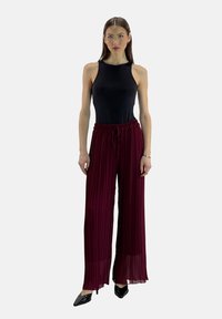 Sort ærmeløs top kombineret med højtaljede, plisserede bordeauxbukser. Bukserne har elastik i taljen og et flydende, bredt bendesign.